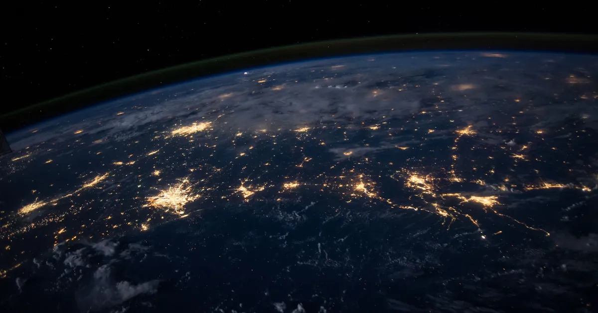 The Earth at night from space, city lights tracing continents against the dark