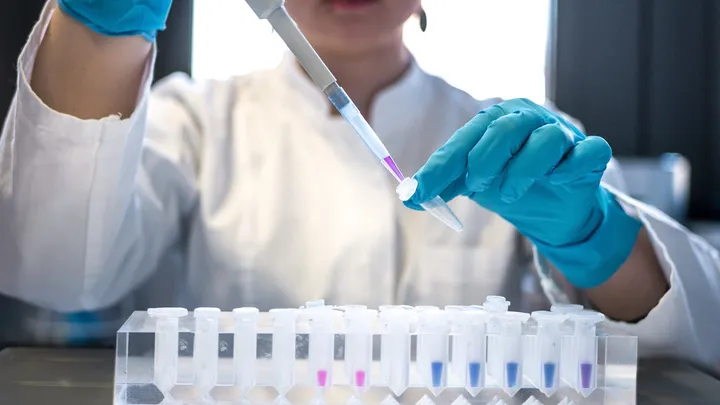 A pipette dispensing liquid into a laboratory tray, representing pharmaceutical research