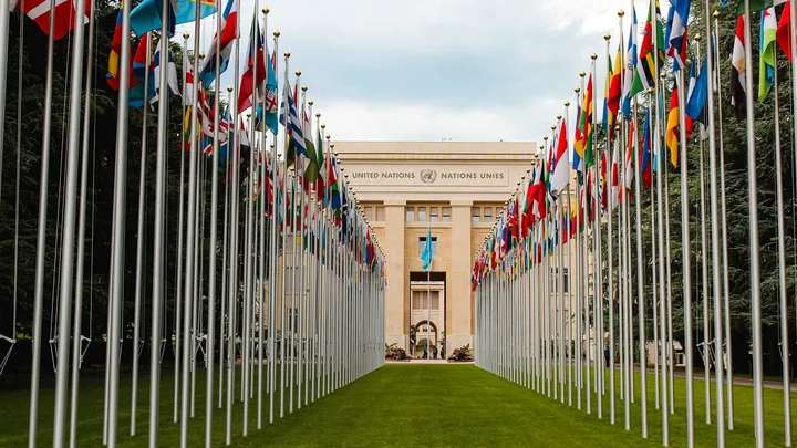 Rows of national flags lining the plaza outside a government building, representing state power and international governance